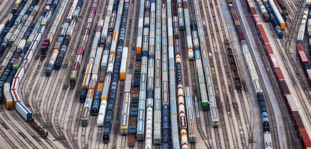 Aerial view of rail yard with lots of converging tracks and different kinds of trains.
